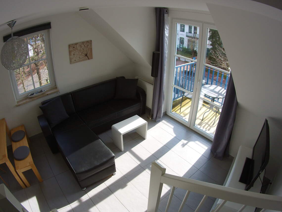 Wohnbereich mit Couch, TV und Sicht auf den Balkon